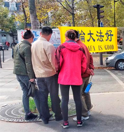 '圖：大陸遊客在巴黎艾菲爾鐵塔真相點觀看揭露中共迫害法輪功的展板。'