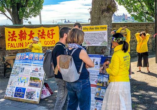 '圖1～2：仲夏節期間法輪功學員頭戴花環人們展示舒緩祥和的法輪功的五套功法，發放真相資料的學員帶著微笑向遊客送上節日的祝福。'