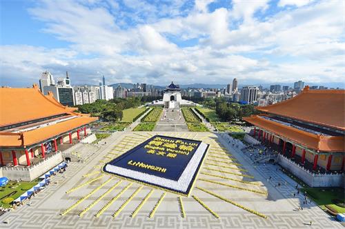 '圖1：二零一八年十一月二十四日，約五千四百名法輪功學員於台北自由廣場排出巨幅的英譯本《轉法輪》：深藍色的書皮、金黃色的書名與作者名、白色的書頁，並綻放四十二道金黃色的光芒，場面壯觀殊勝。'