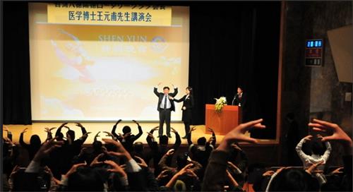 圖4：二零一二年一月十四日，王元甫在東京新宿的會堂演講「不花錢、不吃藥的氣功健康法」。圖為，王元甫在講台上演示法輪功第二套功法──法輪樁法，台下與會者跟著學煉動作。