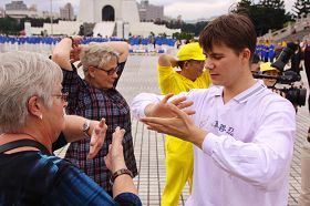 '許多路過的民眾被五套功法美妙音樂所吸引駐足，跟著法輪功學員學煉功法。'