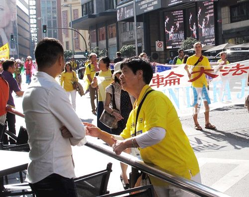 圖4：一位亞裔面孔的男青年正在認真觀看法輪功大遊行，法輪功學員走上前去與他親切交談