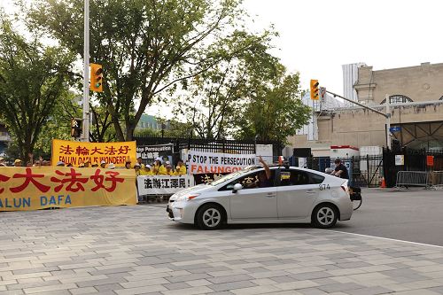 '圖2：一位加拿大人駛過Westin酒店時，向法輪功學員做勝利的手勢。'